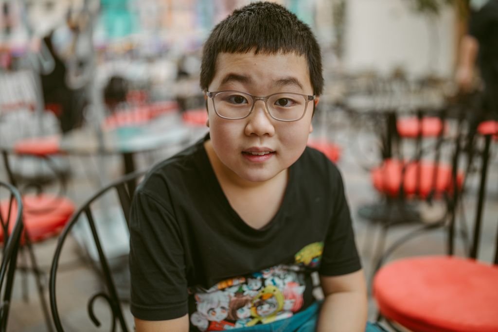 Portrait of a young boy wearing eyeglasses in a casual setting with chairs.